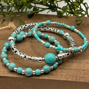 May include: Three turquoise and silver beaded bracelets with intricate silver designs. The bracelets are stacked on top of each other.
