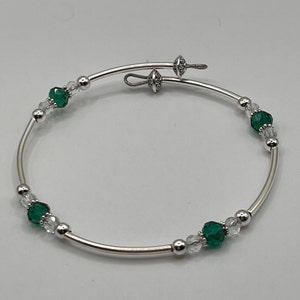 May include: A silver bangle bracelet with a clasp closure. The bracelet is adorned with clear and emerald green crystal beads.