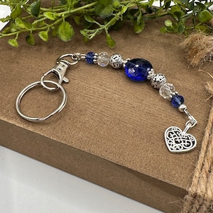 May include: A silver key chain with a blue glass bead, silver beads, and a silver heart charm.