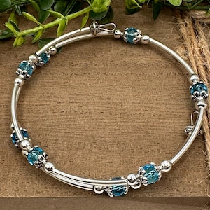 May include: A silver bangle bracelet with two rows of blue beads. The bracelet is open and has a clasp.