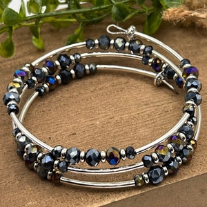 May include: A silver bangle bracelet with three rows of iridescent black beads. The beads are faceted and have a metallic sheen.