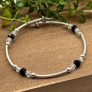 May include: A silver bangle bracelet with alternating black and clear crystal beads.