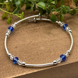 May include: A silver bangle bracelet with clear and blue crystal beads. The bracelet has a hinged clasp.