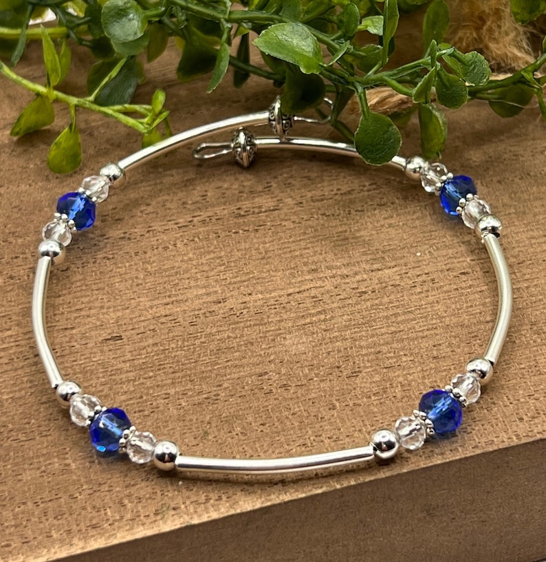May include: A silver bangle bracelet with clear and blue crystal beads. The bracelet has a hinged clasp.