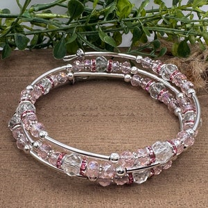 May include: A silver bangle bracelet with three rows of clear and pink crystal beads. The beads are faceted and have a subtle shimmer.