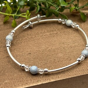 May include: A silver bangle bracelet with a delicate design featuring alternating clear and light blue beads.