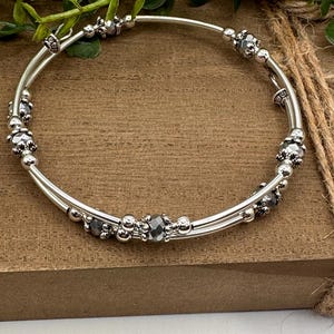 May include: A silver bangle bracelet with two rows of beads. The beads are silver and dark gray.