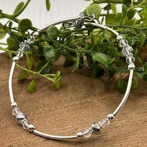 May include: A silver bangle bracelet with clear and silver beads. The bracelet has a silver clasp.