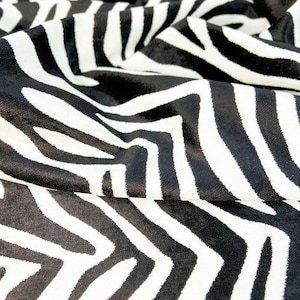 May include: Black and white zebra print fabric with a soft, velvety texture. The fabric is folded and draped, showing the pattern and texture.