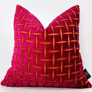 Könnte beinhalten: Ein rosa-oranges Dekokissen mit geometrischem Muster. Das Kissen ist aus Samt und hat einen dezenten Glanz.