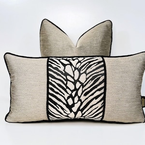 Könnte beinhalten: Zwei dekorative Kissen mit einem schwarz-weißen Zebra-Muster. Die Kissen sind aus beigefarbenem Stoff mit schwarzer Paspel.