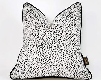 Puede incluir: Almohada blanca con un patrón de lunares negros y un ribete negro. La almohada tiene una etiqueta negra con la palabra "Home" en ella.