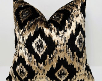 May include: A black and gold velvet pillow with an ikat pattern. The pillow is square and has a soft, plush texture.