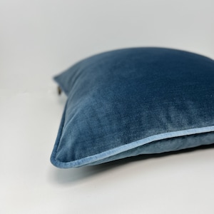 Könnte beinhalten: Ein weiches, blaues Samtkissen mit einer hellblauen Paspel an den Rändern.