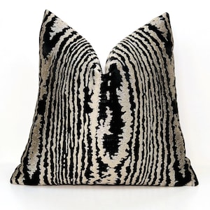 May include: A decorative throw pillow with a black and beige striped pattern. The pillow has a textured surface and a soft, plush appearance. The design features vertical stripes that create a visual texture, suitable for home decor.