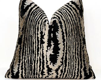 May include: A decorative throw pillow with a black and beige striped pattern. The pillow has a textured surface and a soft, plush appearance. The design features vertical stripes that create a visual texture, suitable for home decor.