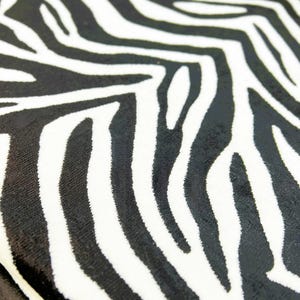 May include: Black and white zebra print fabric with a soft, velvety texture.