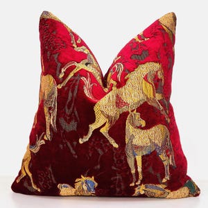 May include: A square throw pillow featuring a deep red velvet base with an intricate woven pattern of golden horses in various poses. The design includes multiple horses depicted in profile and motion, rendered in metallic gold thread against the red.