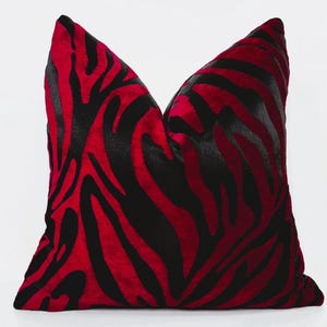 Op de afbeelding: Een rood en zwart kussen met een zebra-achtig patroon. Het kussen is gemaakt van een zachte, pluche stof.