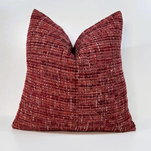 May include: A red and white textured throw pillow with a square shape.