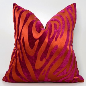 Puede incluir: Una almohada decorativa con un patrón abstracto rosa y naranja. La almohada está hecha de una tela suave y aterciopelada.