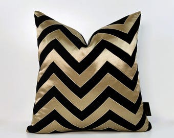 May include: Black and gold chevron patterned throw pillow. The pillow is made of a soft, luxurious fabric and features a bold, geometric design.