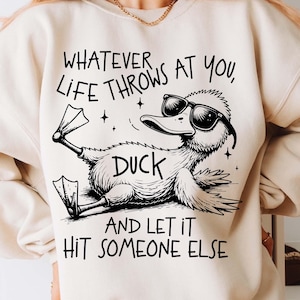 May include: A white sweatshirt with a black graphic of a duck wearing sunglasses and the text "Whatever life throws at you, duck and let it hit someone else."