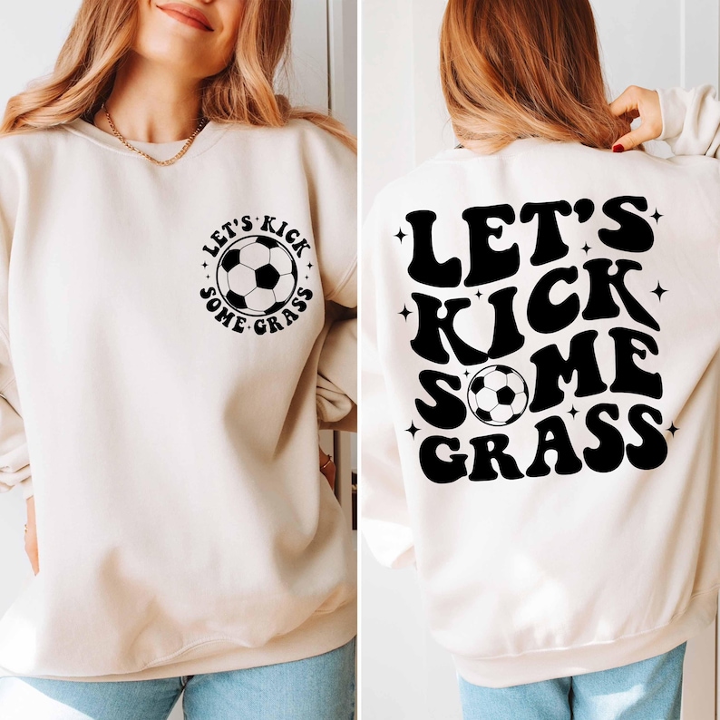 K&ouml;nnte beinhalten: Ein cremefarbener Pullover mit dem Text "Let's Kick Some Grass" in Schwarz, mit einem Fu&szlig;ball-Motiv. Der Text ist in einem Retro-Schriftart-Stil.