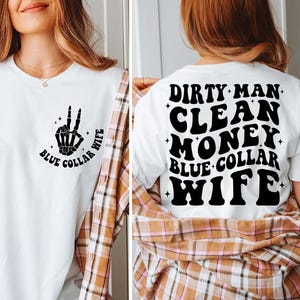 May include: White t-shirt with a black skeleton hand making a peace sign and the text "Blue Collar Wife". The back of the shirt has the text "Dirty Man Clean Money Blue Collar Wife" in black.