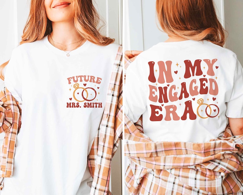 May include: Two white t-shirts with a pink and red graphic design. The first shirt says "Future Mrs. Smith" with a ring design. The second shirt says "In My Engaged Era" with a ring design.