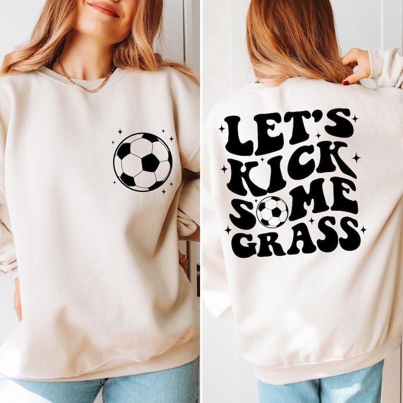K&ouml;nnte beinhalten: Ein cremefarbener Pullover mit einem schwarzen Fu&szlig;ball-Motiv auf der Vorderseite und dem Text "Let's Kick Some Grass" auf der R&uuml;ckseite.