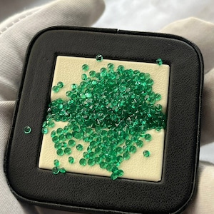 Puede incluir: Una bandeja de cuero negro con un interior blanco contiene una gran cantidad de pequeñas piedras preciosas de color verde brillante.