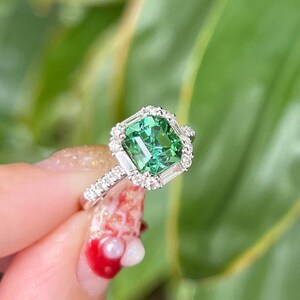 Pu&ograve; includere: Un anello d'argento con una pietra preziosa verde circondata da un'aureola di diamanti pi&ugrave; piccoli.