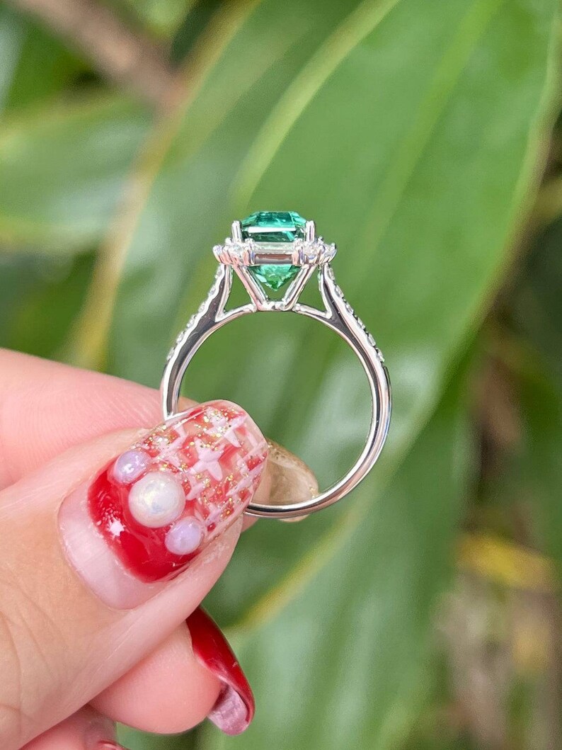 Pu&ograve; includere: Un anello d'argento con un grande smeraldo verde circondato da diamanti pi&ugrave; piccoli. L'anello &egrave; incastonato in stile halo.