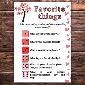 May include: A printable game card with a pink heart tree and dice. The card has the text "Favorite things" and instructions to take turns rolling the dice and sharing something about yourself. The card has six questions, each with a different number of dice, asking about favorite movie, dessert, flower, hobby, place visited, and holiday/celebration day and why.