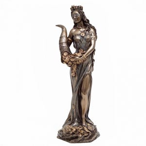 May include: A bronze statue of a goddess holding a cornucopia overflowing with coins. She is wearing a crown and a blindfold, and her dress is flowing. The statue is standing on a base with coins scattered around it.