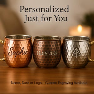 May include: Three copper mugs with personalized engravings. The mugs are hammered and have a shiny finish. The first mug is engraved with the name "Sophie", the second mug is engraved with the date "12.06.2024", and the third mug is engraved with a small tree design.