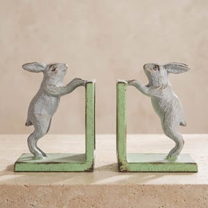May include: A pair of bookends featuring two rabbits standing on their hind legs, each with their front paws resting on a vertical support. The rabbits are finished in a light gray color, while the L-shaped bases are painted in a light green.