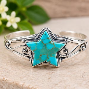 May include: A silver cuff bracelet featuring a central star-shaped turquoise stone with brown matrix veining. The metal band displays intricate scrollwork and swirling wire details on both sides of the star, creating a polished, open-ended design.