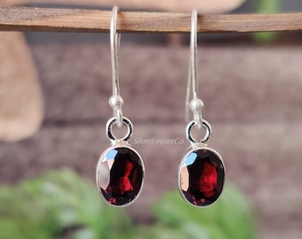 May include: A pair of silver dangle earrings featuring oval-shaped red garnet gemstones. The earrings have a simple design and are ideal for everyday wear.