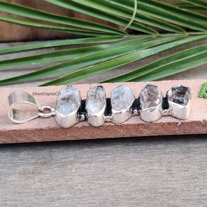 Pu&ograve; includere: Ciondolo in argento con cinque punte di cristallo di quarzo trasparente incastonate in argento, con un'anellina in argento. Il ciondolo &egrave; su una superficie marrone. SilverEmpireCo &egrave; visibile nell'immagine.