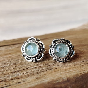 May include: A pair of silver earrings with a light blue gemstone in each. The earrings have a detailed, ornate design.