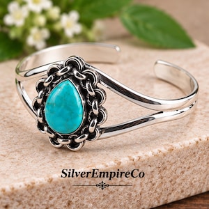 May include: A silver cuff bracelet featuring a central teardrop-shaped turquoise stone surrounded by a decorative scalloped metal border. The band is split into two polished silver arms. The text SilverEmpireCo is printed at the bottom.