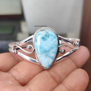 Pode incluir: Pulseira de punho de prata com uma grande pedra de larimar em forma de pêra. A pedra é azul clara com marmoreio branco. A pulseira tem um design vazado. Circunferência de aproximadamente 17 cm.