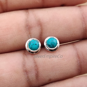 以下が含まれることがあります： ターコイズストーンが付いたシルバーのスタッドピアスのペア。ピアスは丸型で、シルバーのベゼルセッティングが施されています。