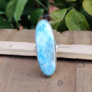 May include: A silver ring with a large oval-shaped blue and white gemstone. The gemstone has a swirling pattern and a light blue color.