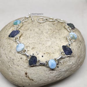 Può includere: Un braccialetto a catena d'argento con pietre preziose blu e verdi alternate. Il braccialetto ha una chiusura a moschettone.