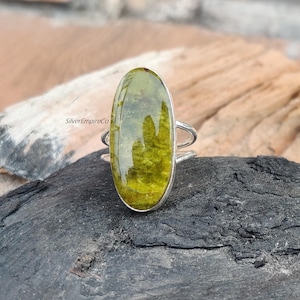 May include: A silver ring with a large oval green gemstone. The gemstone has a mottled, marbled appearance.