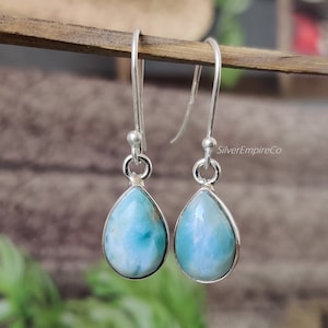 May include: A pair of silver teardrop earrings with blue and white gemstone drops. The earrings are on a wooden surface.