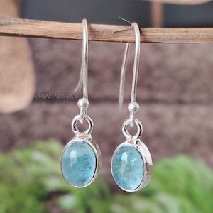 May include: A pair of silver dangle earrings featuring light blue oval-shaped gemstones. The earrings have a simple design and are ideal for everyday wear.